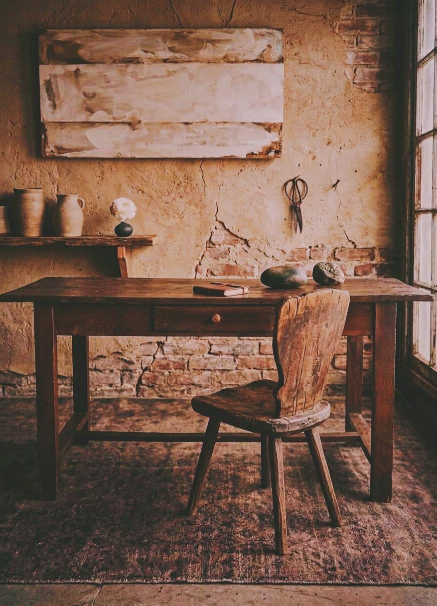 The Hawthorn Desk, antique wooden desk with a single drawer in a rustic plaster and brick room, primitive wood chair, faded rug, tall window light