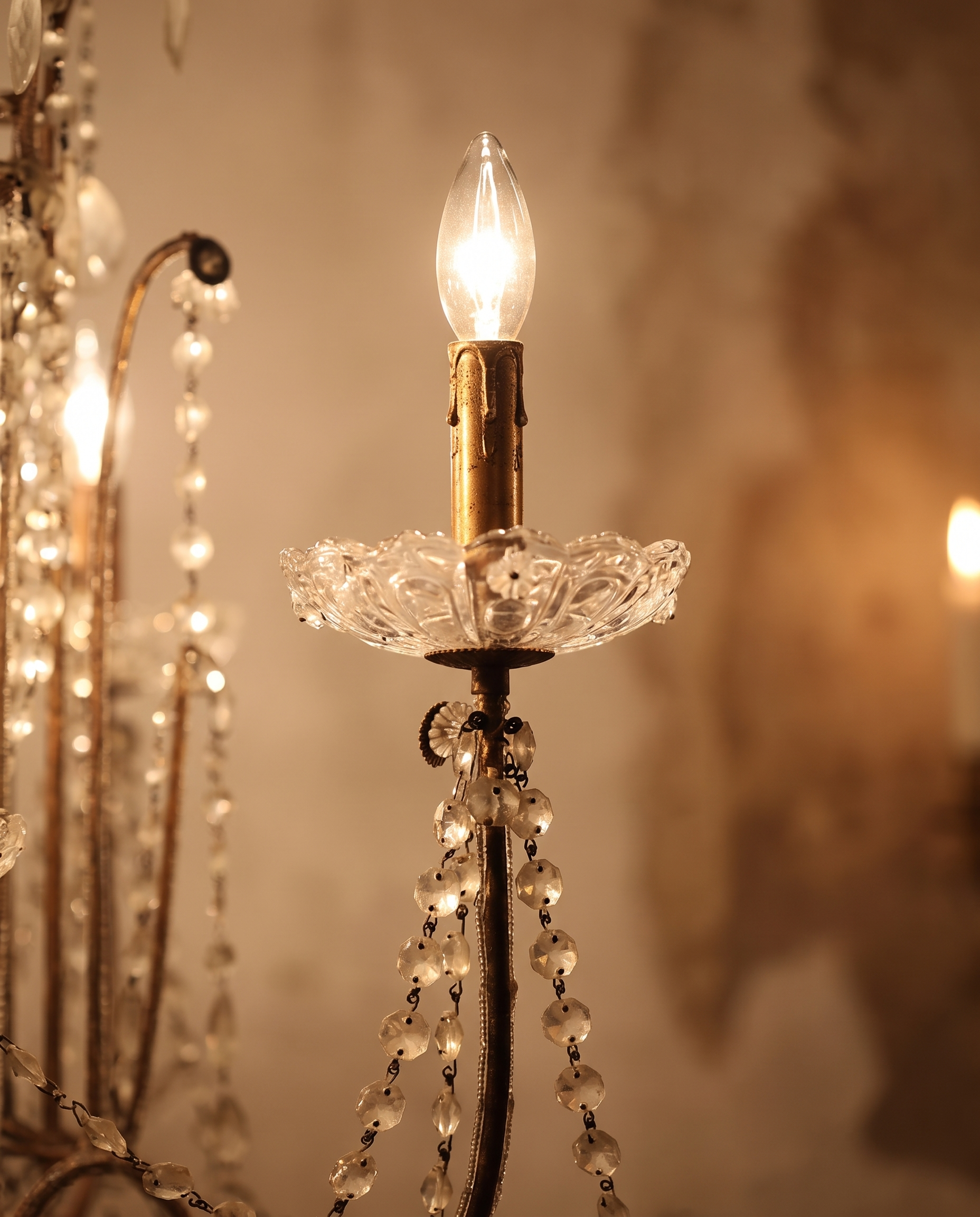 Detail of a candelabra arm with cut-glass floral bobeche and upright lit flame-tip bulb