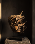 Senufo sacrifice mask on a stone plinth in a dark gallery alcove, warm raking light