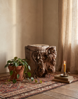 Carved teak temple capital styled on the floor on an antique kilim with a plant and candle
