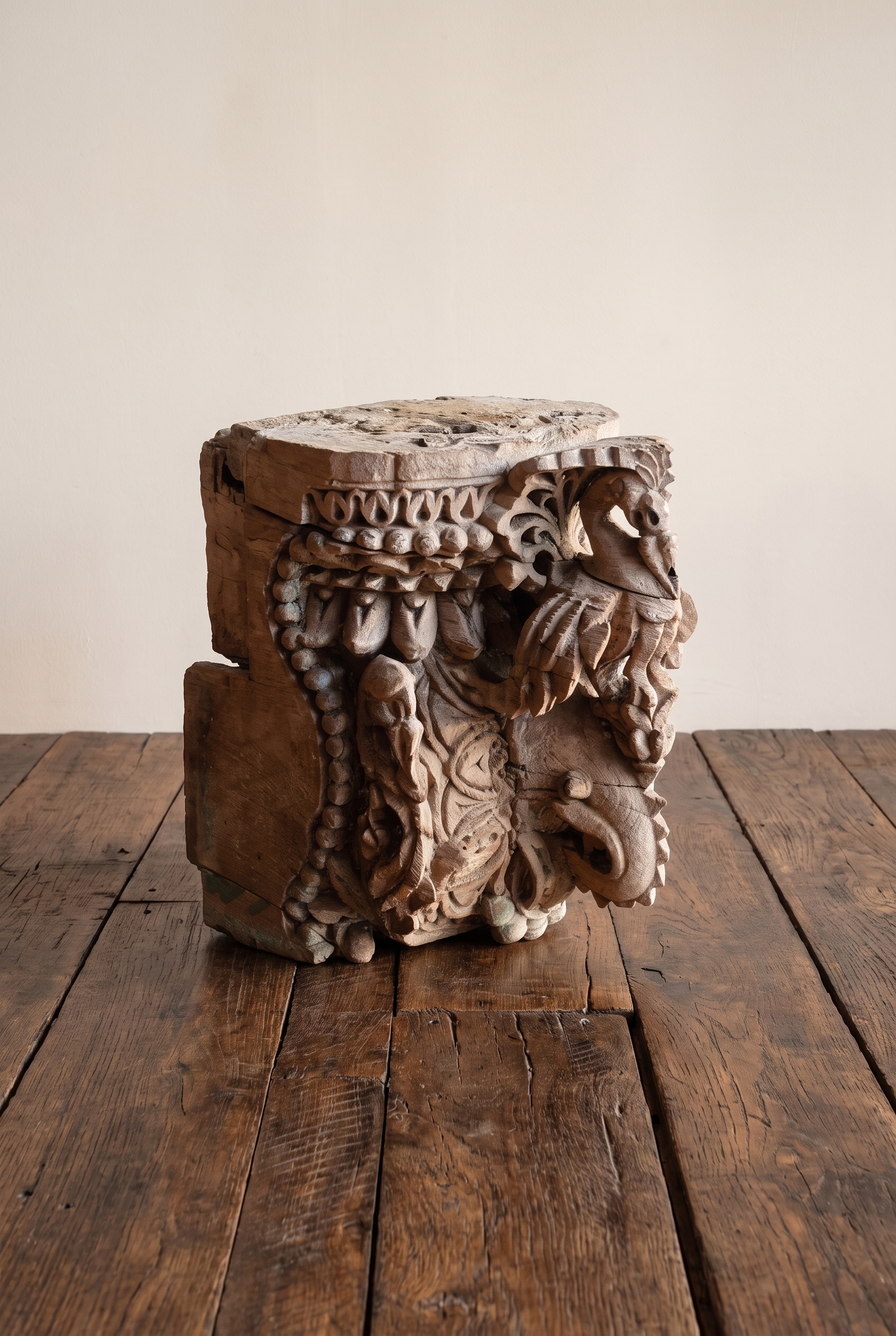Carved teak temple capital, three-quarter view, on a reclaimed wood floor