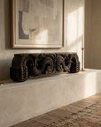 Antique carved wood piece on a plaster mantel beneath a large framed artwork