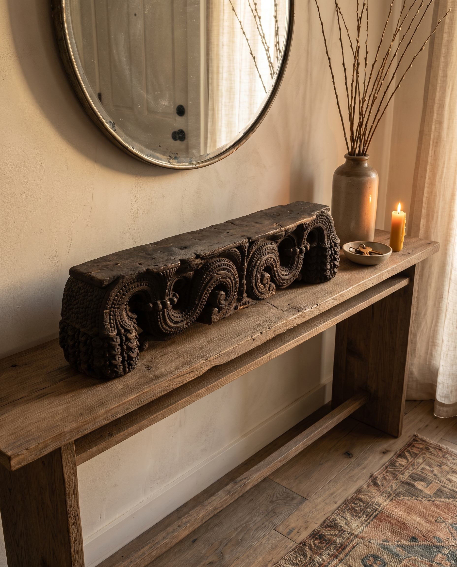Antique carved wood piece on an entryway console beneath a round mirror