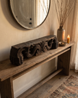 Antique carved wood piece on an entryway console beneath a round mirror