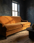 Cognac velvet sofa in a dark plaster room under a tall window, candlelit