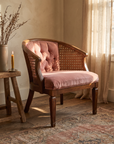Dusty rose velvet cane barrel chair beside a rustic side table and candle