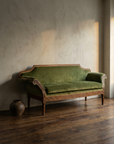 Vintage carved-frame green velvet sofa against lime-washed plaster wall in amber light