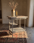 Antique spool table, dramatic-light hero on a kilim rug