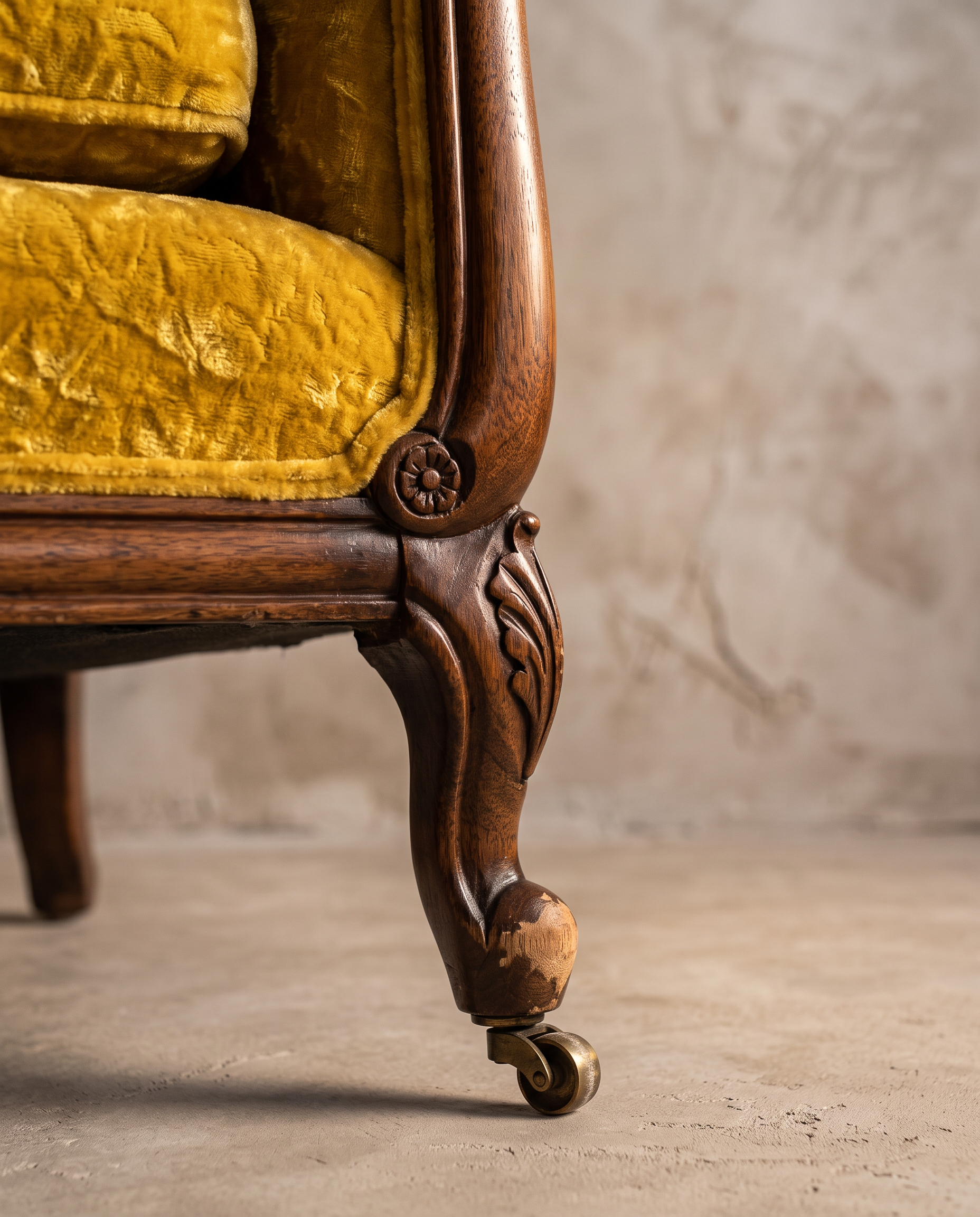 Construction detail of the carved arm, cabriole leg, and brass caster on the vintage gold velvet sofa