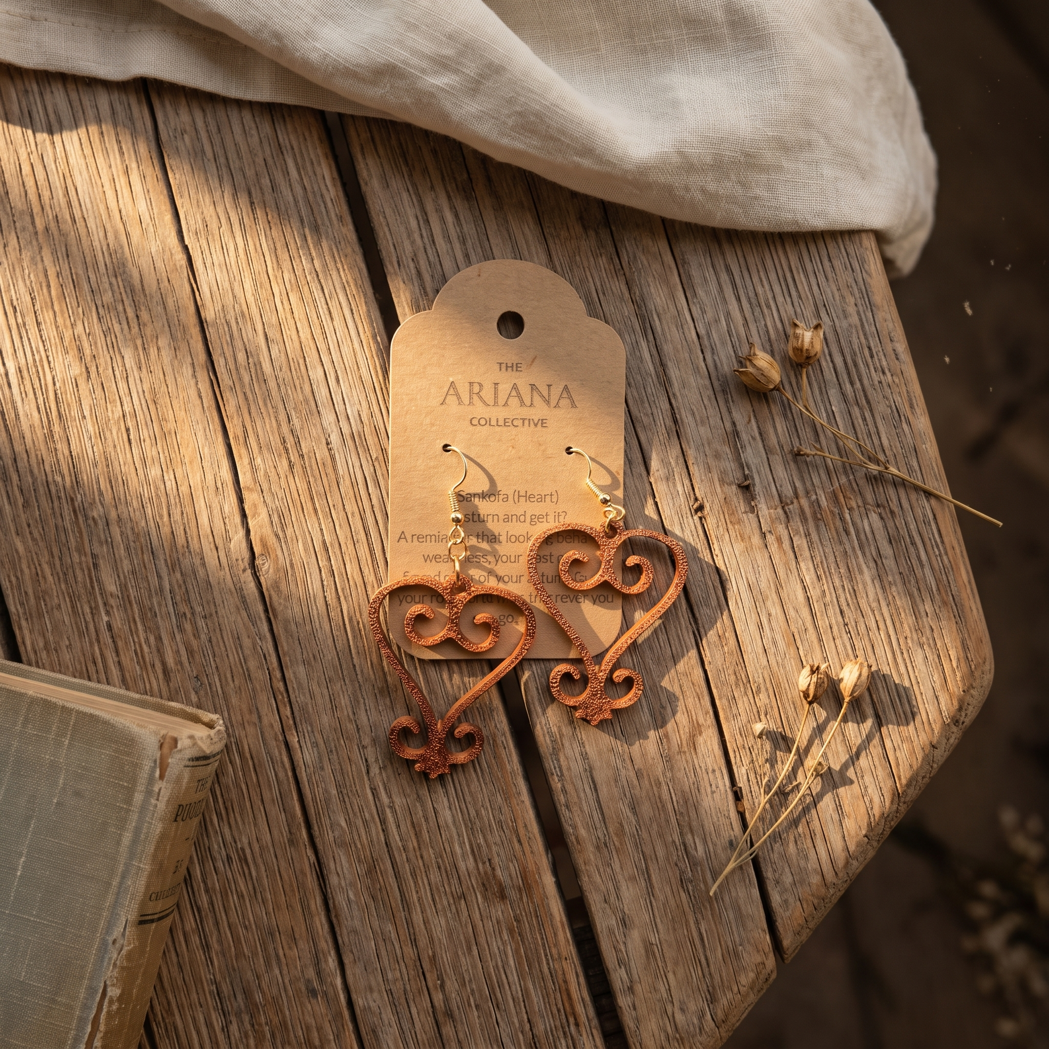 Sankofa heart Adinkra earrings in copper on a kraft Ariana Collective card, on a weathered oak table