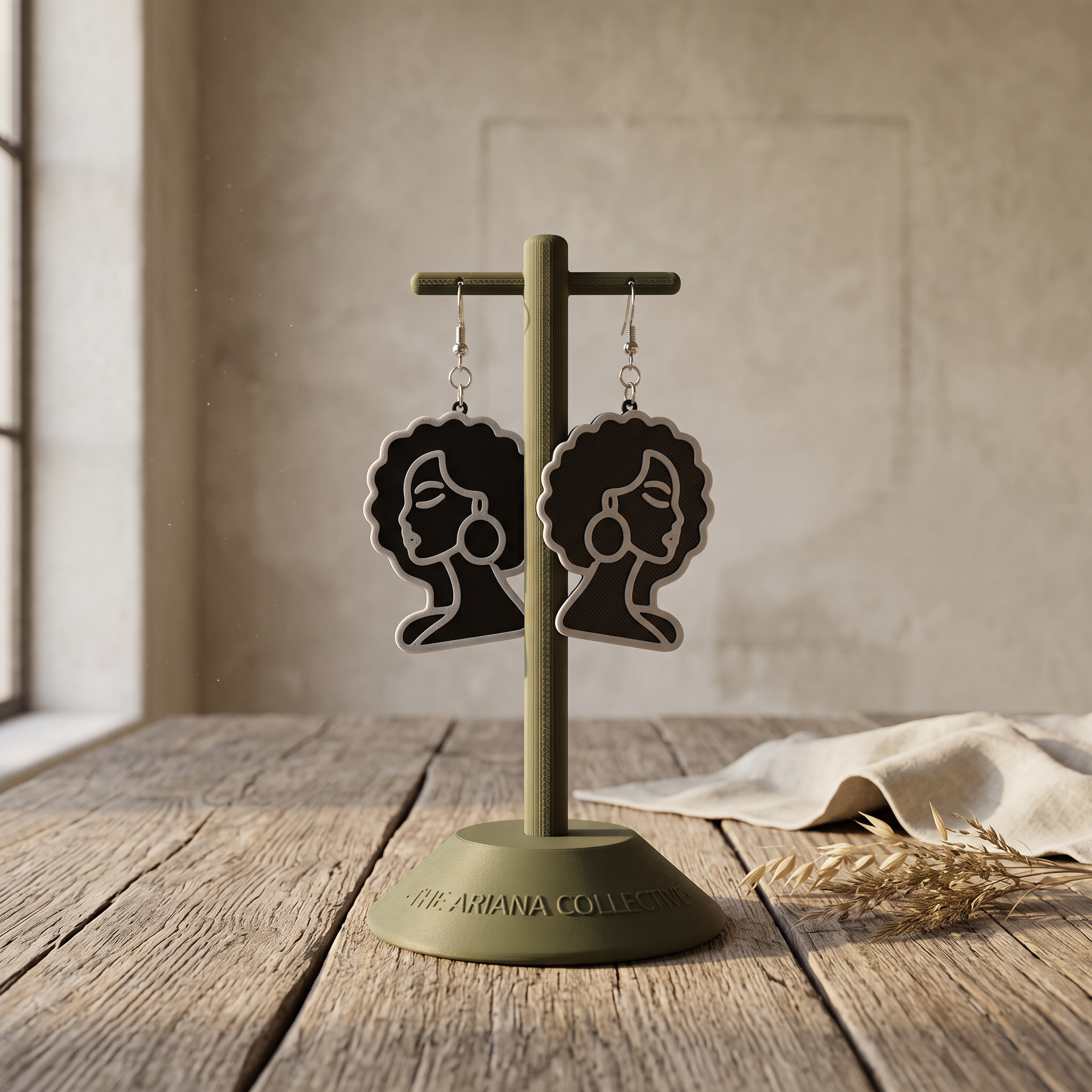 She's Got It earrings, a woman's profile in silhouette, hanging on an olive Ariana Collective stand on a weathered oak table