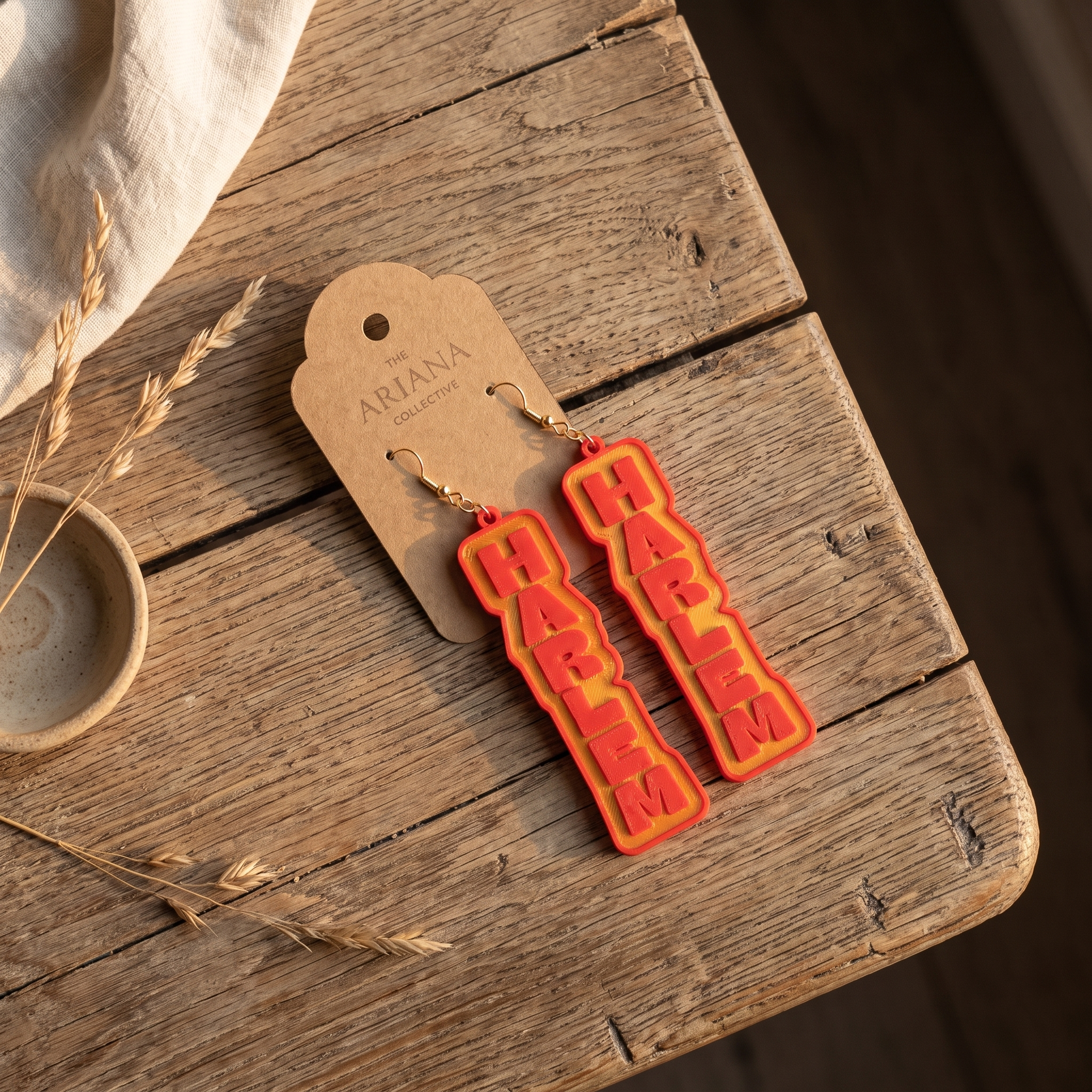 Harlem lettering earrings laid flat with their Ariana Collective card on a weathered oak table