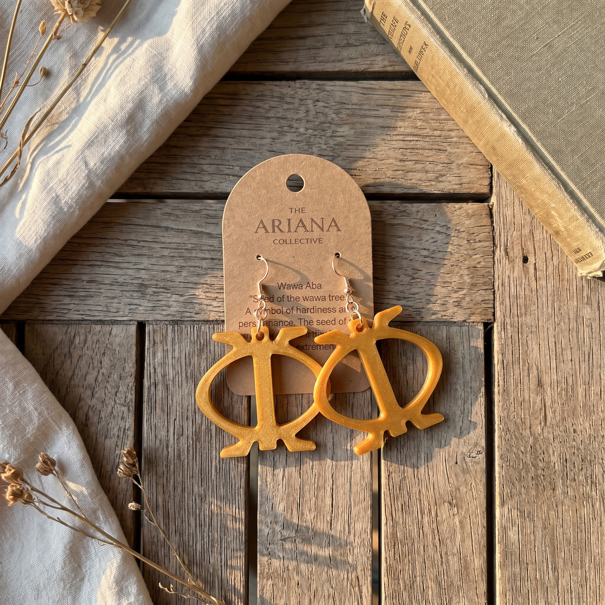 Wawa Aba Adinkra earrings laid flat with their Ariana Collective card on a weathered oak table