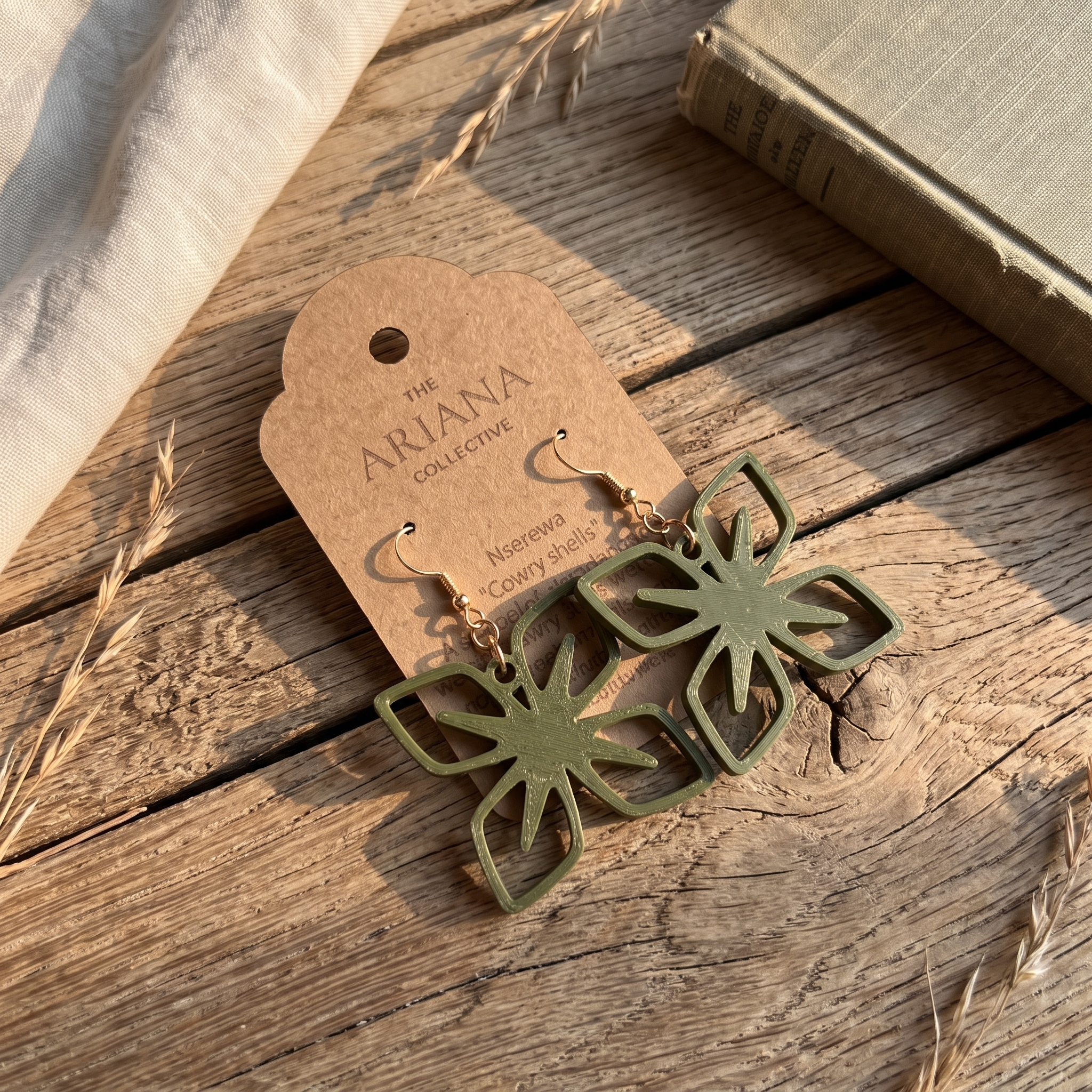 Nserewa cowry shell Adinkra earrings laid flat with their Ariana Collective card on a weathered oak table
