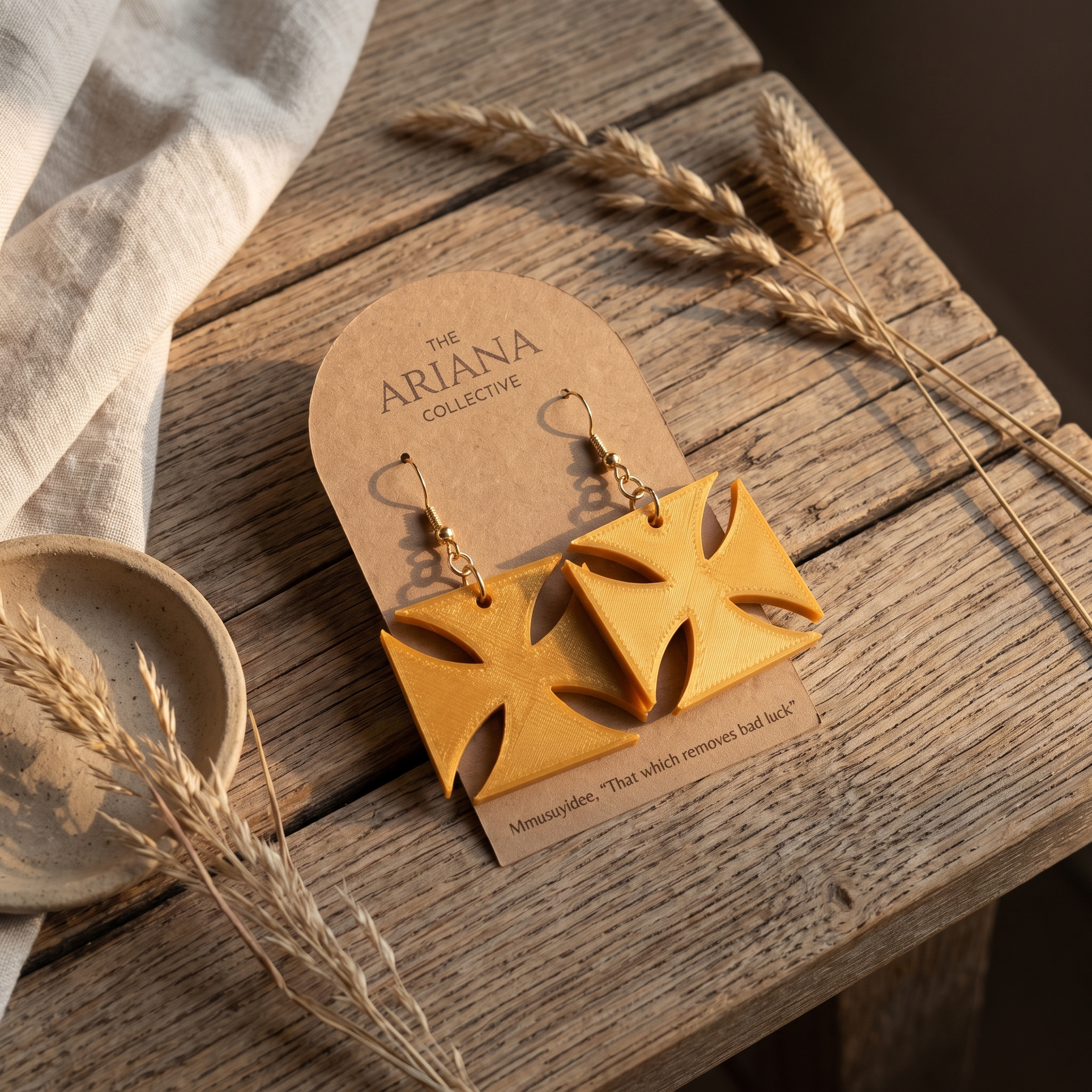 Mmusuyidee Adinkra earrings laid flat with their Ariana Collective card on a weathered oak table