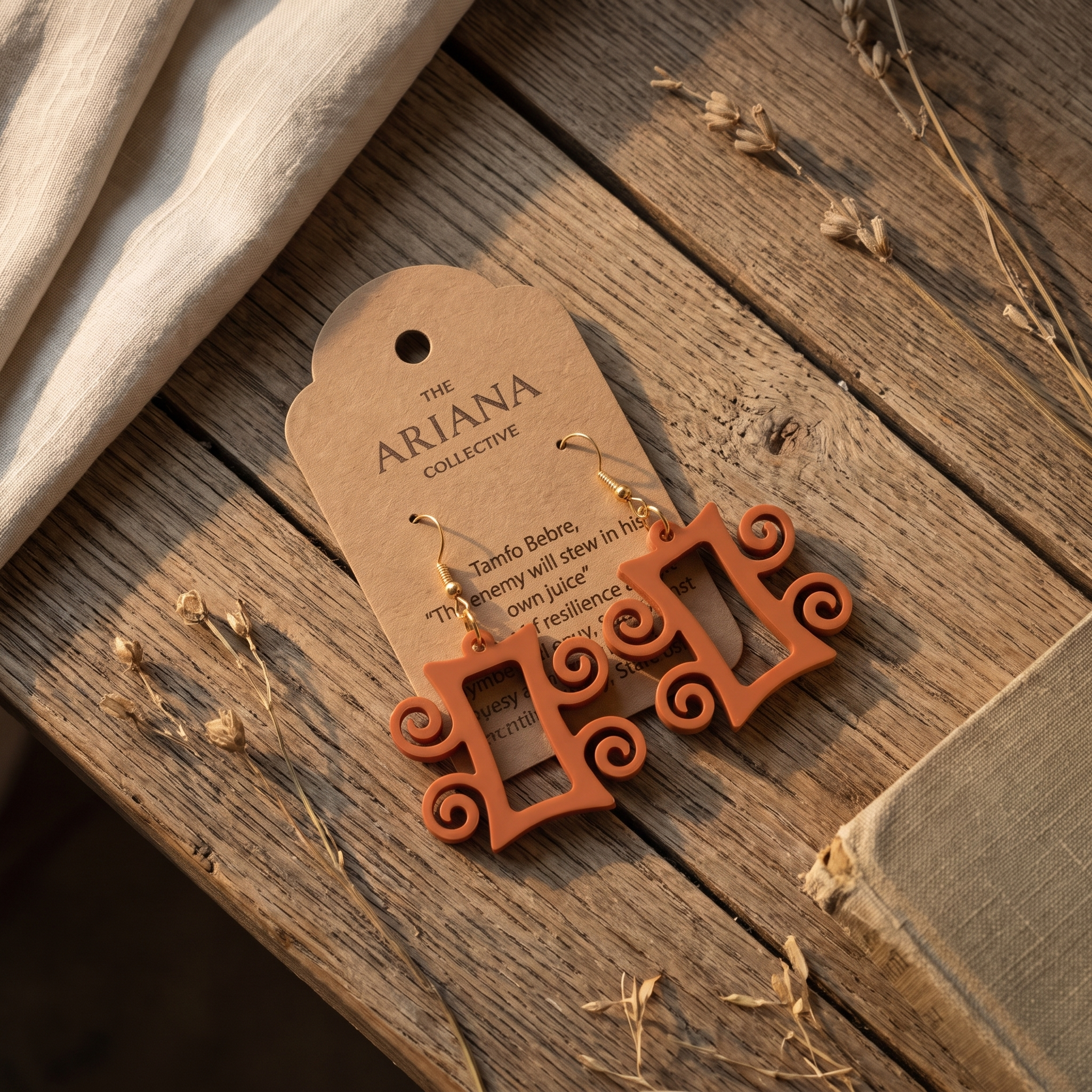 Tamfo Bebre Adinkra earrings laid flat with their Ariana Collective card on a weathered oak table