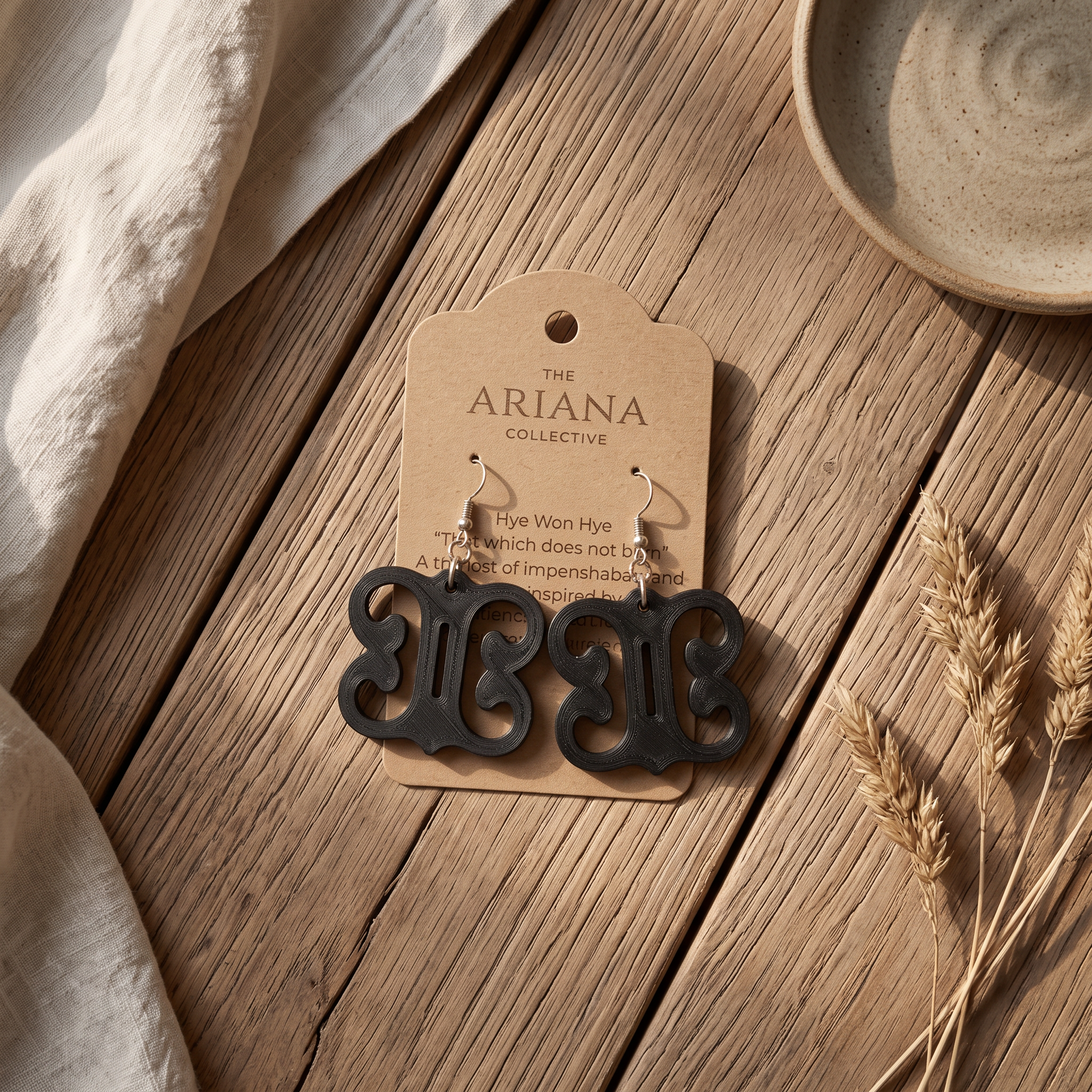 Hye Won Hye Adinkra earrings in black laid flat with their Ariana Collective card on a weathered oak table