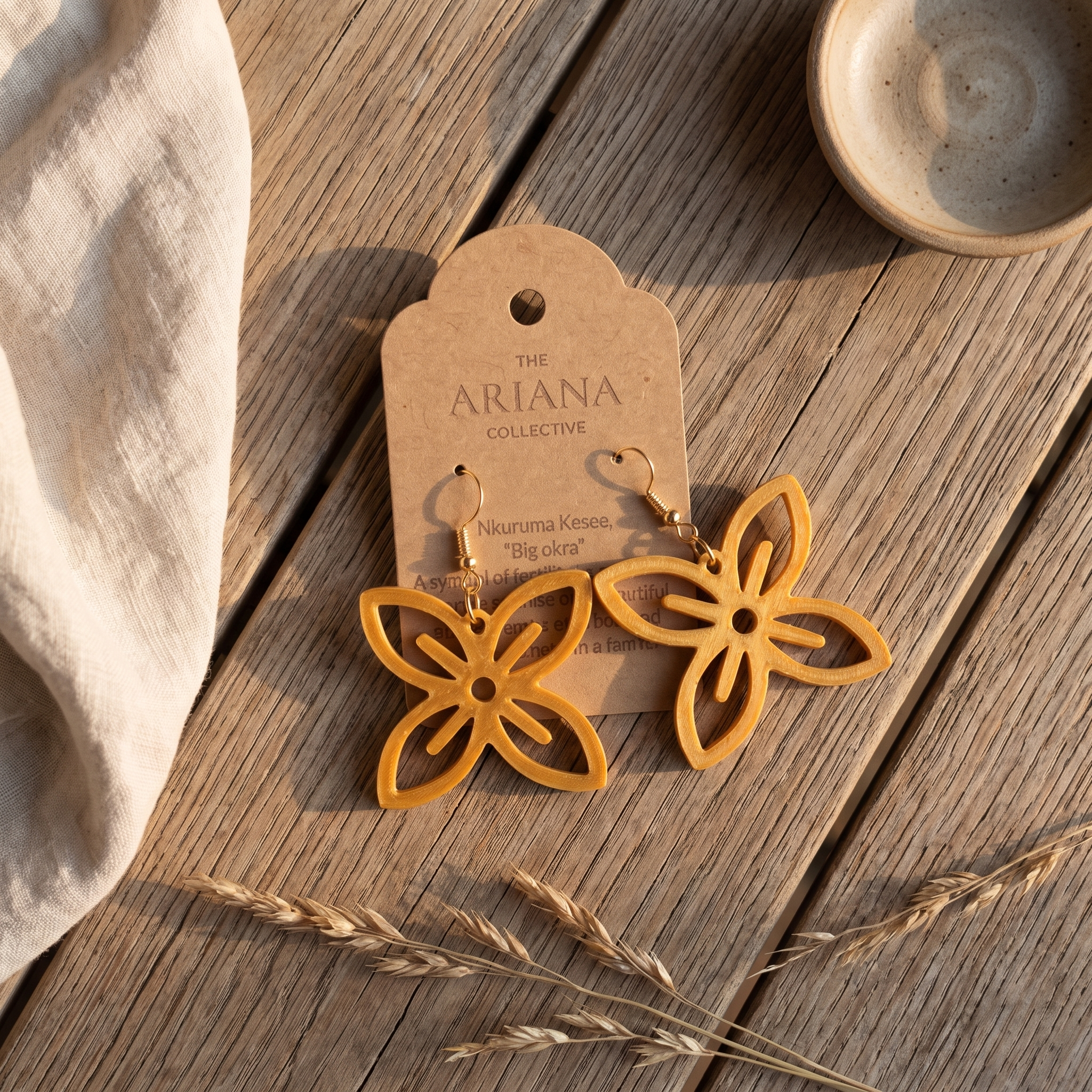 Nkuruma Kesee Adinkra earrings laid flat with their Ariana Collective card on a weathered oak table