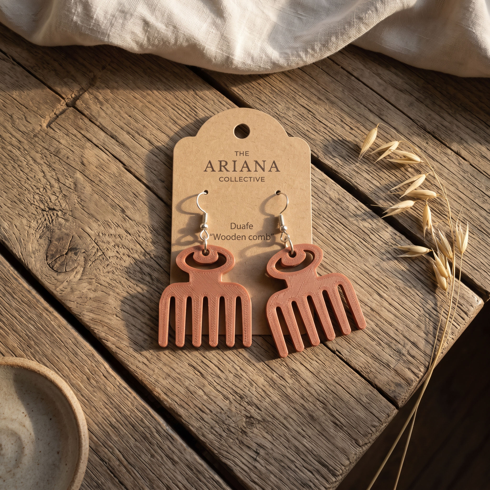 Duafe wooden comb Adinkra earrings laid flat with their Ariana Collective card on a weathered oak table