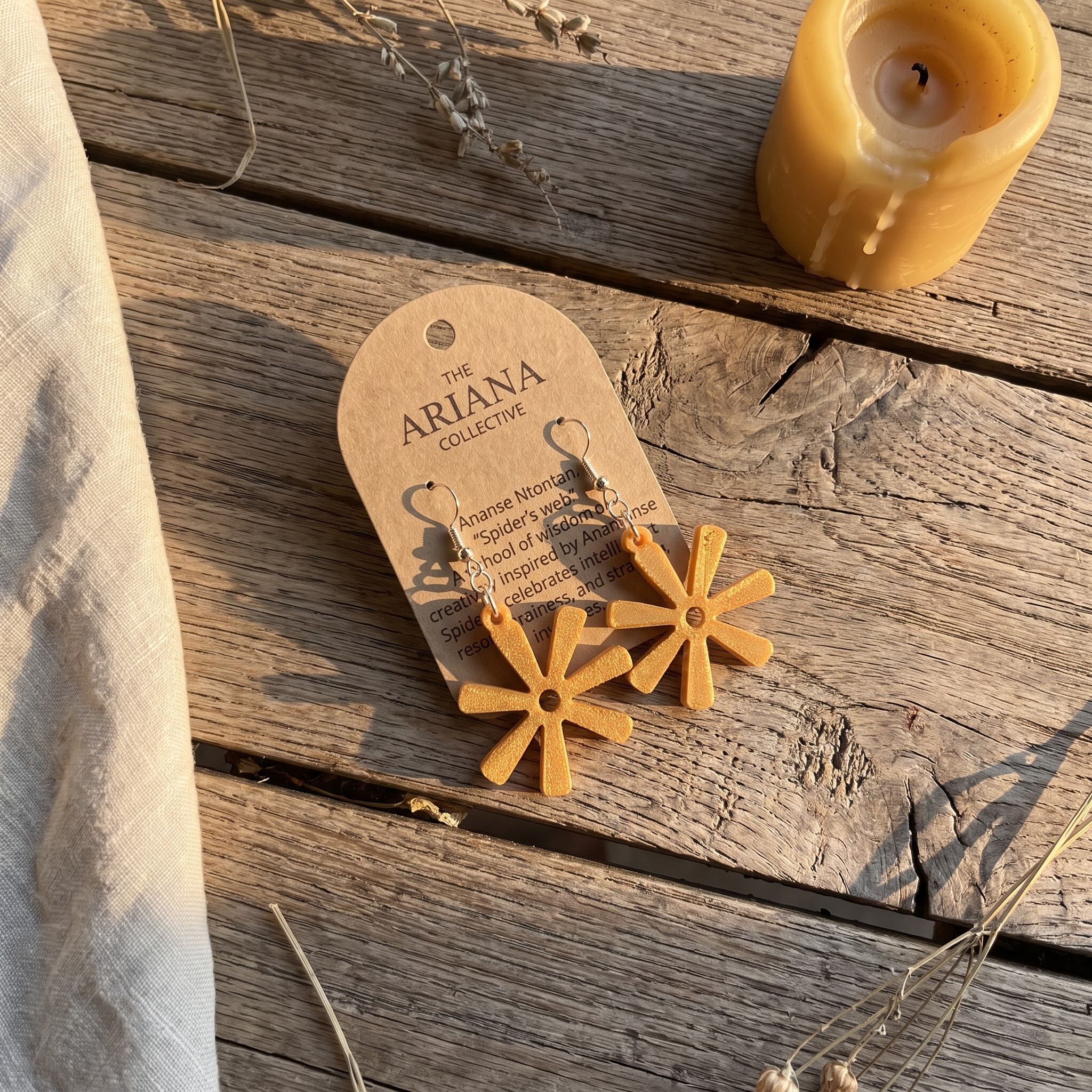 Ananse Ntontan spider's web Adinkra earrings laid flat with their Ariana Collective card on a weathered oak table