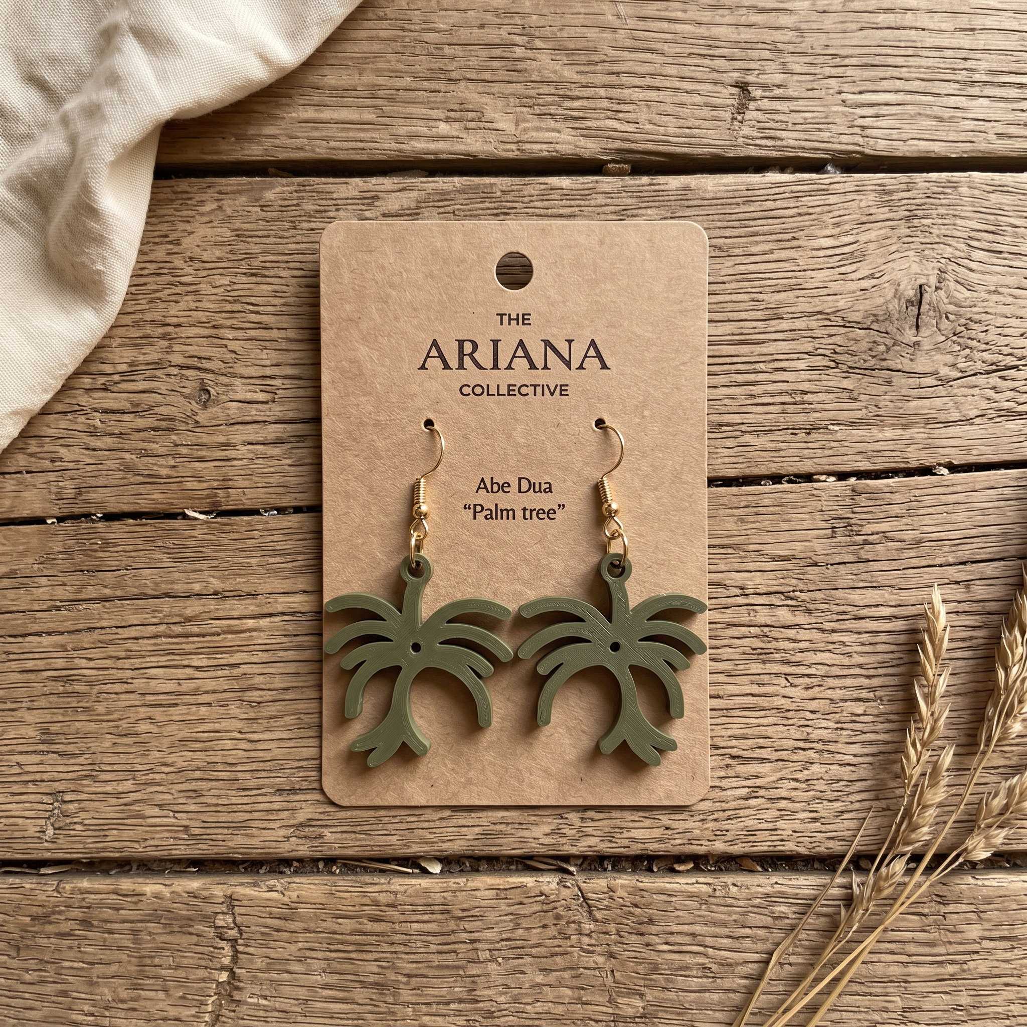 Abe Dua palm tree Adinkra earrings in olive green on their Ariana Collective card, laid flat on a weathered oak table