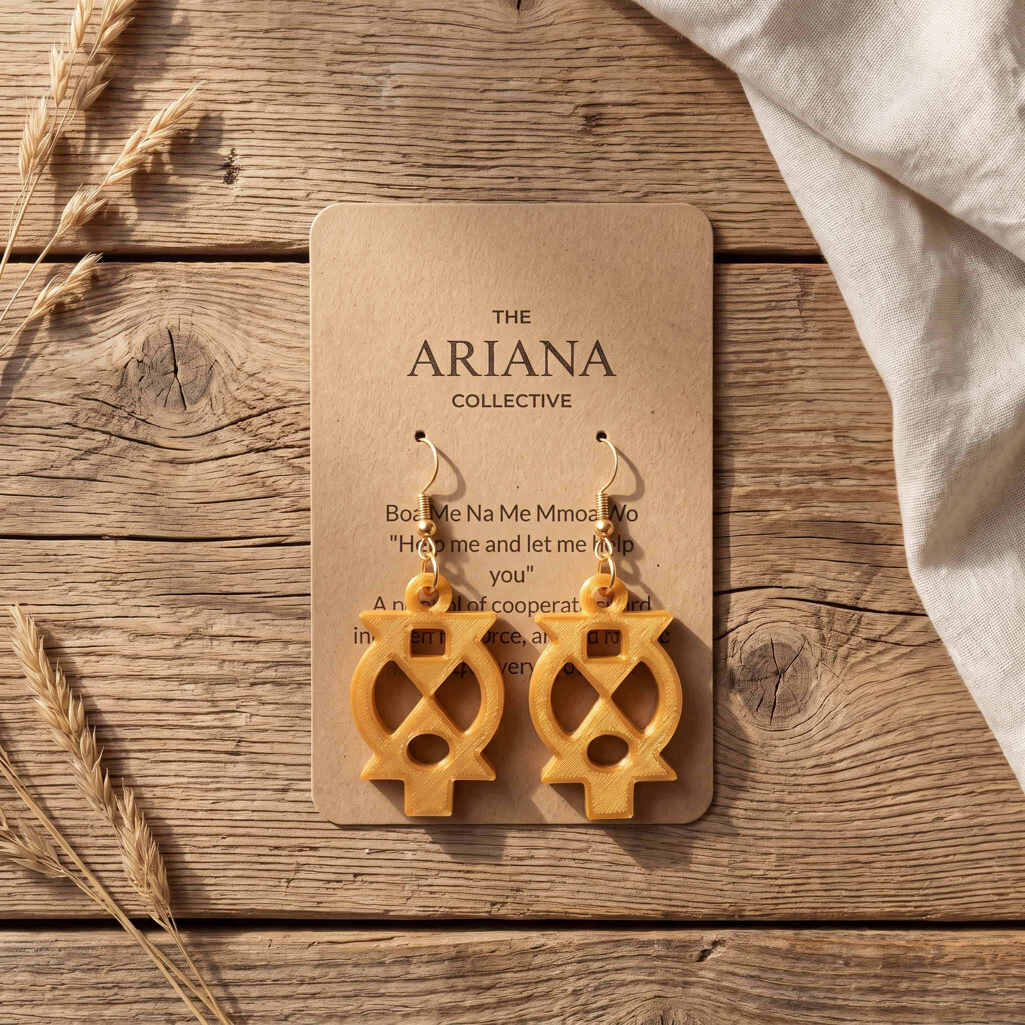 Boa Me Na Me Mmoa Wo Adinkra earrings in gold on their Ariana Collective card, laid flat on a weathered oak table