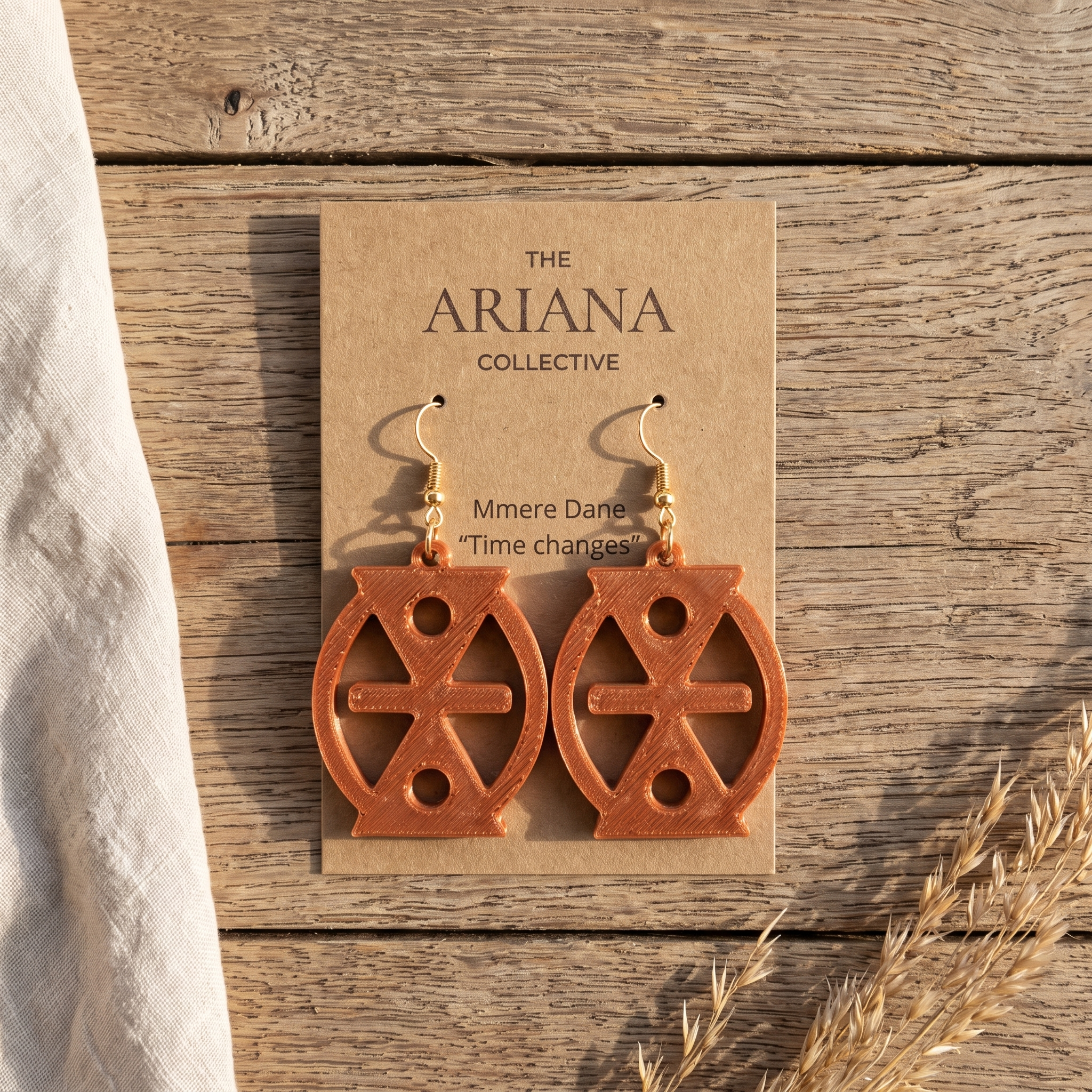 Mmere Dane Adinkra earrings in terracotta on their Ariana Collective card, laid flat on a weathered oak table