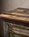 Macro detail of The Verdigris Chest top surface and molded edge, showing weathered patchwork grain