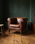Vintage whiskey leather club chair, lifestyle shot, dark green plaster wall, reclaimed wood floor