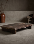 North India bajot, low antique teak riser table, staged in a raw greige plaster room with stoneware vessels and dried branches