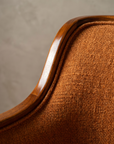 Macro detail of the walnut wood arm rail and woven burnt orange upholstery