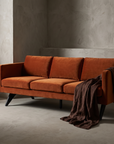 Burnt orange velvet boomerang-leg sofa, lifestyle shot in a greige plaster room with stoneware vessels and draped chocolate linen