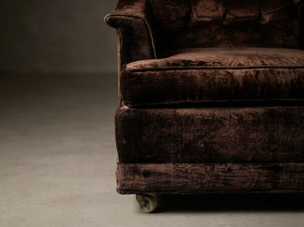 Front corner detail showing the rolled arm cap, welted seat cushion edge, plinth base band and original front caster