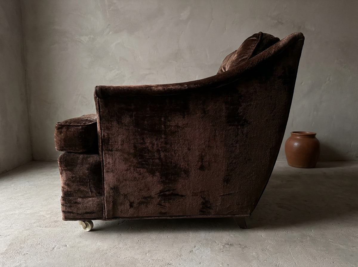 Side profile of the chocolate velvet club chair showing the concave sweep of the outside back from top rail down to the base