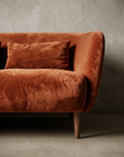 Close detail of the sofa seat cushion, low curved arm, rust lumbar pillow and slim tapered walnut leg