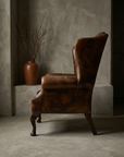 Side profile of the leather wing chair showing the depth of the wing, the rolled arm and the cabriole front leg