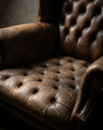 Macro of the deeply button-tufted leather seat, creased and sat-in, meeting the rolled arm