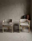 Both sueded white armchairs facing the viewer with the Antique Grate Side Table between them in a greige plaster room