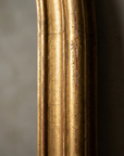 Macro detail of the gilt molding along the straight side of the mirror frame, rubbed through to red bole at the high points