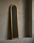 Three-quarter angled view of the slim arched giltwood mirror resting on a plaster ledge, showing the depth of the molding profile