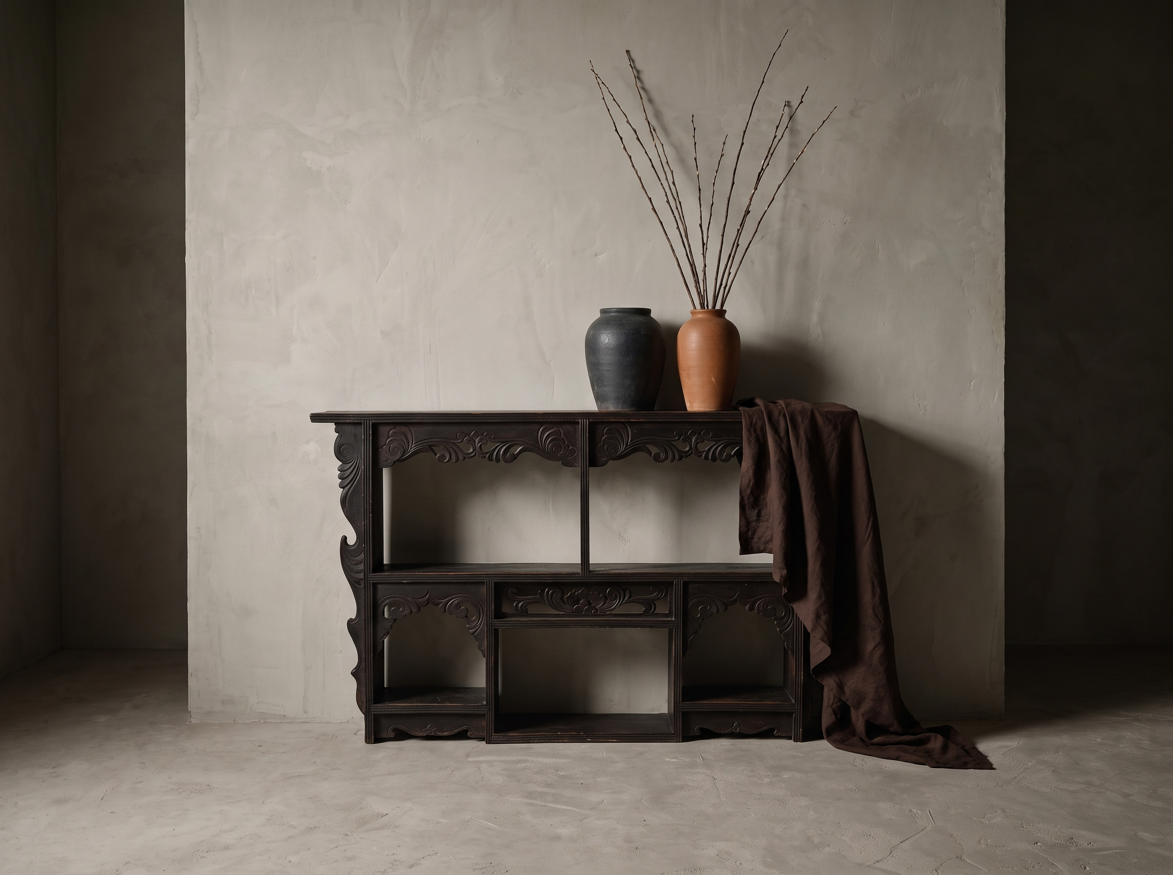 Antique carved black wall shelf shown at true scale against a tall greige plaster wall with stoneware vessels and draped linen