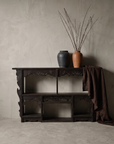 Antique carved black wall shelf shown at true scale against a tall greige plaster wall with stoneware vessels and draped linen