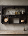 Antique carved black wall shelf mounted above a kitchen counter, styled with glass herb jars and pu-erh tea cakes
