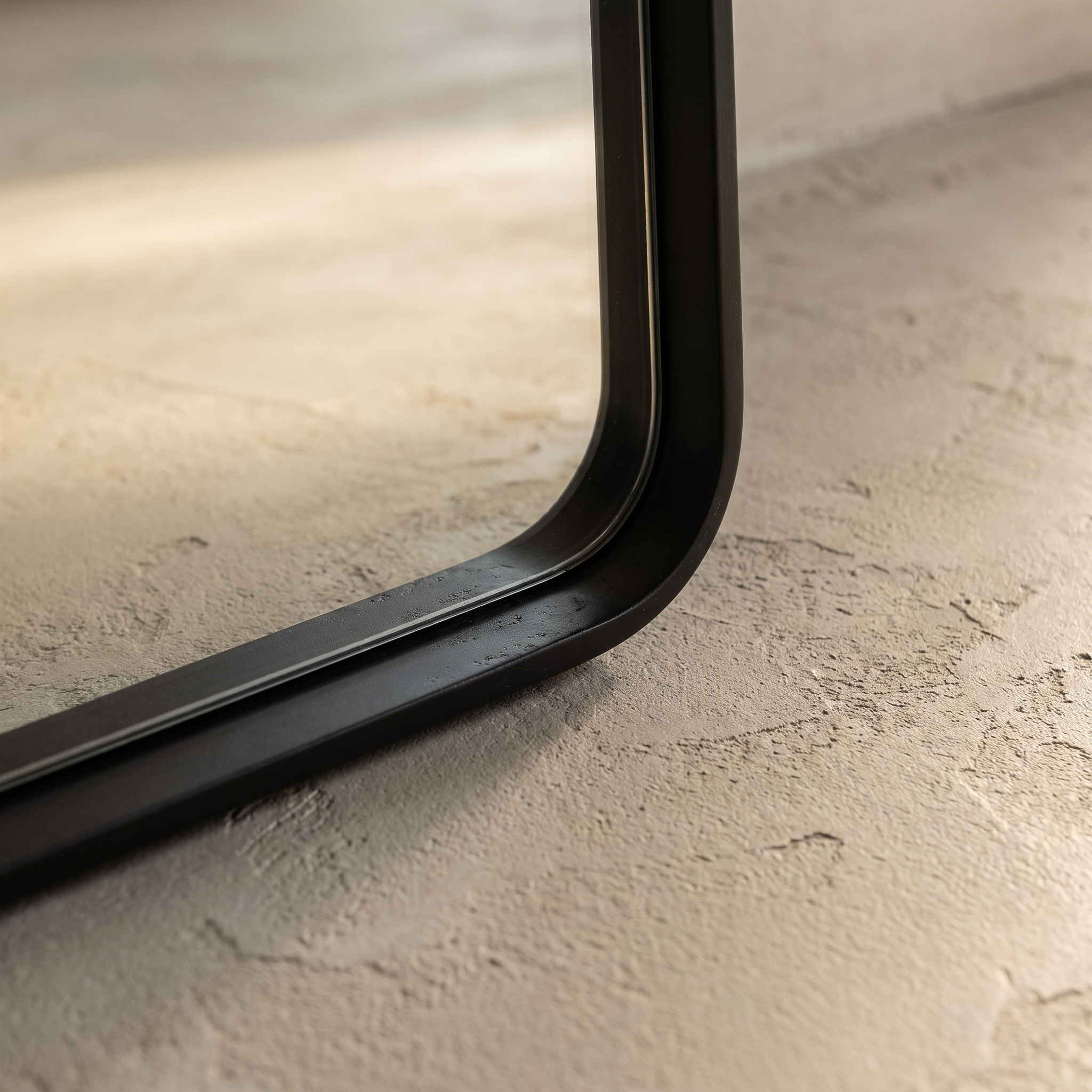 Macro detail of the mirror's bottom corner showing the matte black frame profile and rounded join