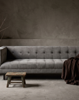 Blue-grey velvet biscuit-tufted sofa in a greige plaster room, lifestyle hero shot