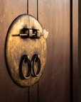 Macro detail of the round brass medallion lock plate and ring pulls, matte dark oxblood finish