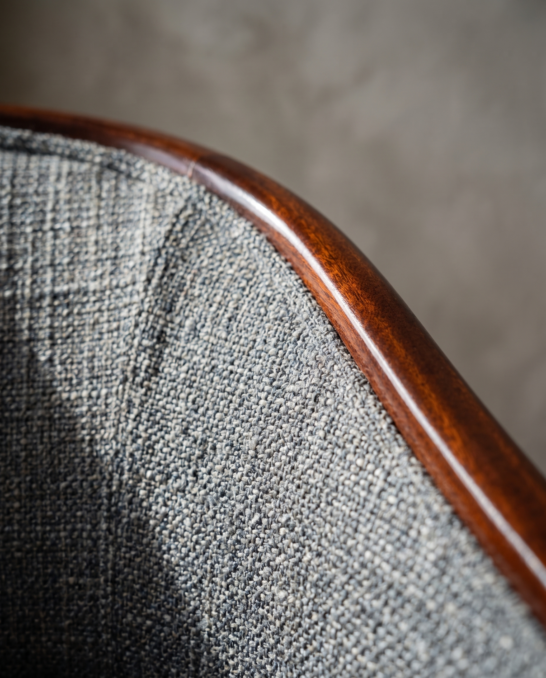 Macro detail of the grey-blue bouclé weave and mahogany trim at the seat corner