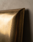 Macro detail of the brass mirror's folded corner and speckled antiqued patina