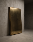 Brass panel mirror leaning against a greige plaster wall, unlacquered brass with speckled antiqued patina