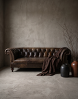 The Umber Chesterfield, vintage leather Chesterfield sofa, vertical lifestyle hero shot in a greige plaster room, matte worn leather